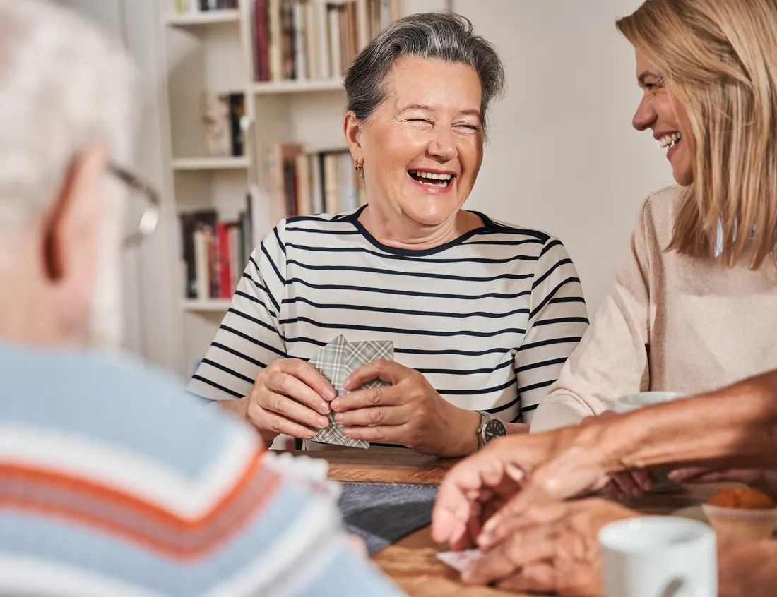 A senior woman and her daughter laughing together at the kitchen table
